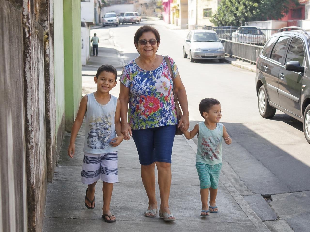 Mulher madura caminhando com os netos em uma rua tranquila. Imagem ilustrativa.